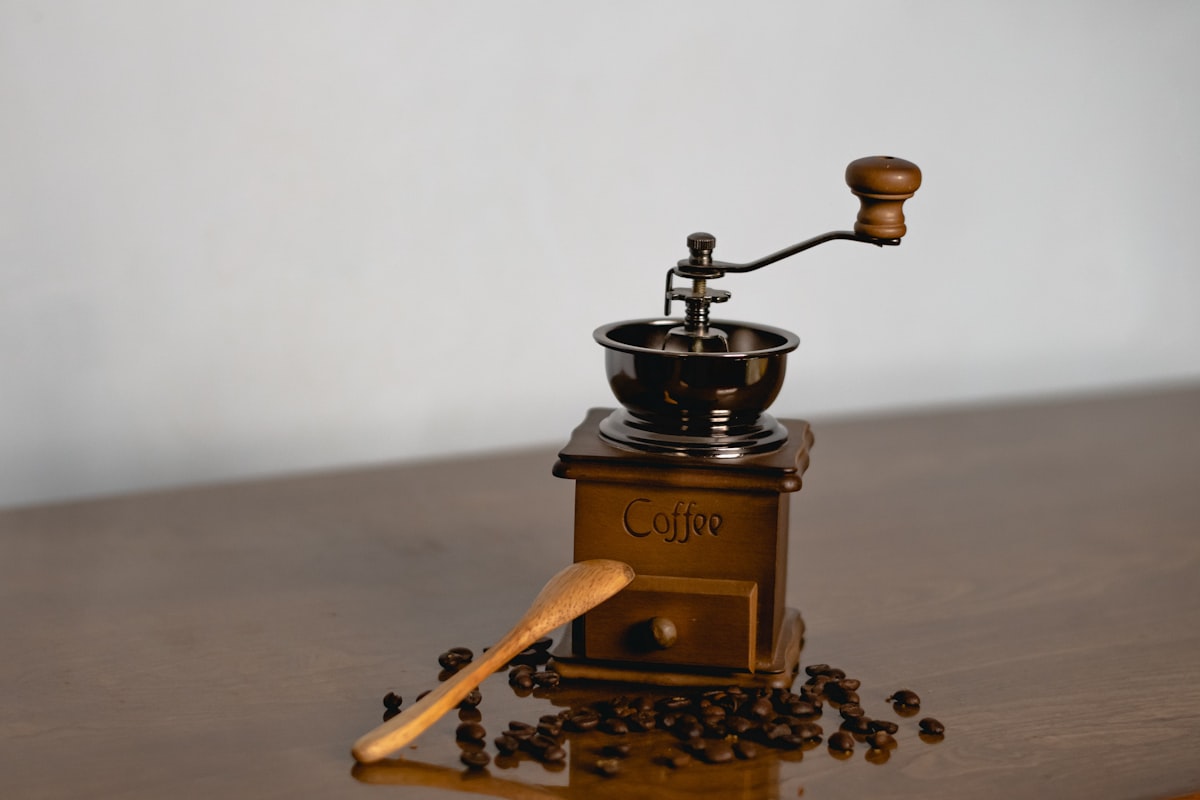 Manual coffee grinder with beans and wooden spoon on a surface